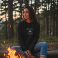 Woman in black Freedom Travel sweatshirt by campfire in forest - Outdoor adventure lifestyle