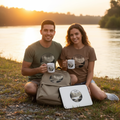 Couple in military green and brown savanna Time by the River t-shirts with backpack, laptop sleeve and ceramic mugs at riverside sunset