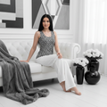 Elegant woman with long dark hair in geometric tank top with white wide leg pants on sofa
