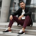 Fit man sitting on steps in red joggers white sweatshirt with black geometric shoes white sole in focus