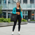 Woman in black athletic wear with teal jacket carrying Adventure Freedom Travel tote bag